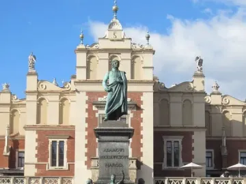 Adam Mickiewicz Monument in a paved square, with bronze figures on a tall pedestal and an ornate building behind it.