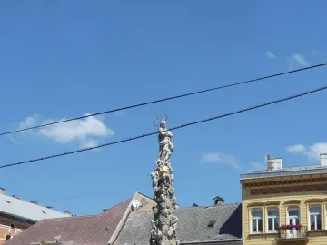Marian Column with a haloed statue of the Virgin Mary, surrounded by figures and a metal fence.