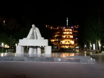 Monument to Alexander Tamanyan at night with the illuminated Cascade complex in the background.