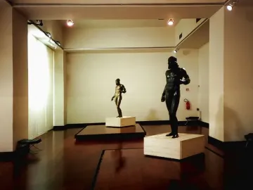 Two Riace bronzes standing on pedestals in a museum gallery.