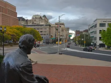 Seated Lincoln overlooks a brick-paved plaza toward a city intersection.
