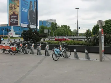 Bicycle rental station with docked bikes on a paved city square.