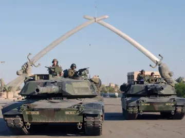 Victory Arch in Baghdad, with two tanks positioned beneath the crossed swords monument held by giant sculpted hands.