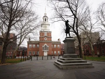 Commodore John Barry statue on a stepped stone pedestal in front of a historic brick building with a clock tower.