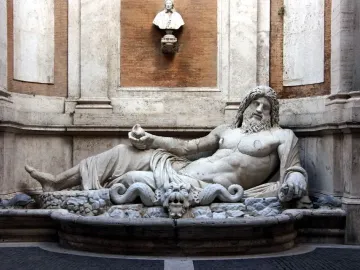 Marforio, a white marble reclining river god with a bearded upper body, set in an architectural niche.