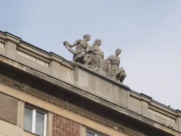 Stone sculpture of three figures representing Music, seen from below against a clear sky.