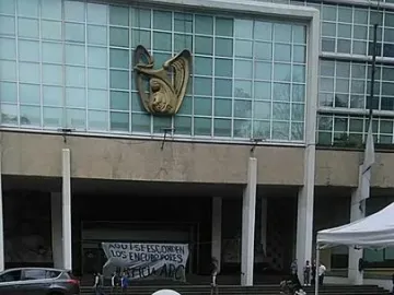 The Antimonumento 49 ABC stands on a building facade above a plaza with red flower petals and a white balloon on the ground.