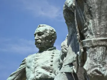 Close-up of the bronze General Philip Sheridan statue with a green patina against a blue sky.