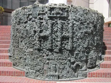 San Francisco Fountain with a highly textured metallic surface and intricate raised details in front of a red-brick platform.