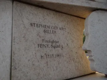 Stone monument engraved with Stephen Gerard Siller’s name and firefighter details beside a sculpted human face profile.