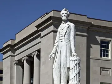 Abraham Lincoln statue on a stone pedestal in front of a classical courthouse building.