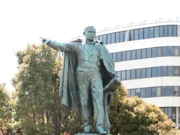 Bronze statue of Benito Juarez standing on a multi-tiered stone pedestal, holding papers and pointing forward.