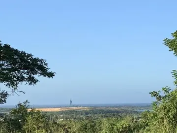 The Birth of the New World sculpture silhouetted against a clear blue sky, with trees in the foreground and water below.