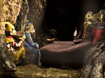 Carved figures inside the Elfin Oak, including a jester, a bearded king in blue, and colorful elf-like characters gathered around a table.