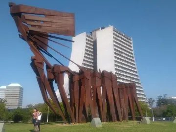 The Monument to the Azoreans, a tall reddish-brown metal sculpture on a grassy lawn with modern buildings behind it.