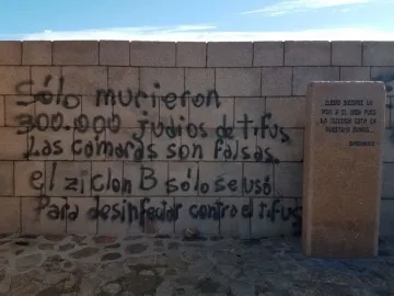 Graffiti-covered wall at the Holocaust Memorial in Uruguay beside a stone pillar with engraved text.