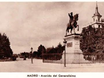 Marqués del Duero monument beside a wide tree-lined avenue in Madrid, with a fence and buildings in the background.