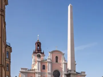 The Obelisk at Slottsbacken stands on a dark tiered pedestal beside a pink and white church with a clock tower.