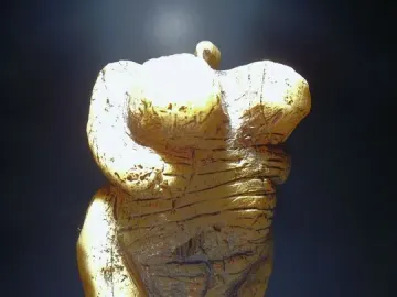Venus of Hohle Fels figurine with pronounced breasts, rounded abdomen, and a loop-like top against a dark background.