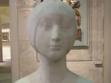White marble bust of a princess with downcast eyes and a simple bob hairstyle, displayed in a museum gallery.