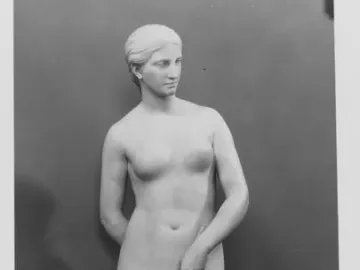 Marble statue of a nude woman standing on a round base and holding a looped rope.