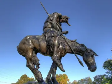 End of the Trail bronze statue of a slumped rider on horseback holding a spear, with bowed heads against a blue sky.