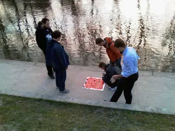 Five men stand beside the Keyboard Monument, looking at a large red panel with raised square blocks laid on a concrete path near the water.