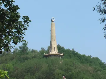 The Thanksgiving Candle monument rises from a wooded hill under a clear blue sky.
