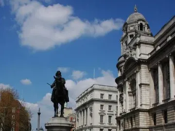 The Duke of Cambridge equestrian statue silhouetted against a grand stone building and blue sky.