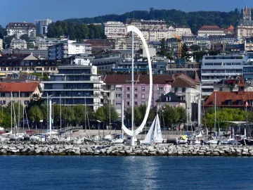Éole, a large white curved sculpture on a rocky breakwater beside sailboats in a marina.