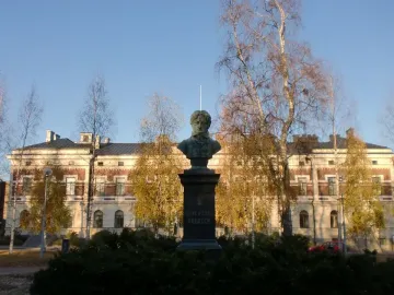 Frans Michael Franzén monument on a tall pedestal beside shrubs and trees in front of a grand building.