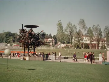 Heureka kinetic sculpture standing on a lawn with visitors nearby and trees in the background.