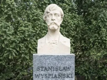 Stanisław Wyspiański bust on a speckled stone pedestal in a wooded outdoor setting