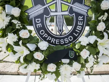 A memorial wreath with white and pale pink flowers, centered on a black Special Forces emblem and a black beret at America\'s Response Monument.