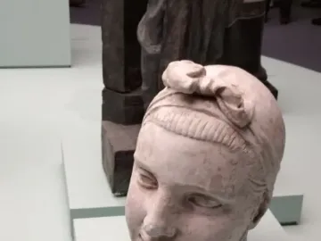 Head sculpture of Girl with an Oar with a decorative bow on top and a pale green pedestal.
