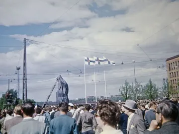 Crowd gathered around the covered Marshal Mannerheim equestrian statue during its unveiling, with flags overhead and a ladder beside it.