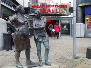 Monument to the Unknown Woman Worker with two bronze women standing outside a shopping mall entrance.