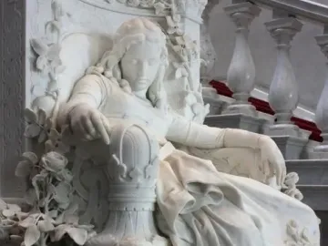Sleeping Beauty marble sculpture of a reclining woman with closed eyes, set in an ornate flower-carved seat.