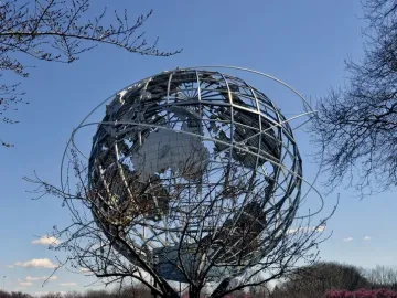 The Unisphere metal globe sculpture with orbital rings against a blue sky, framed by bare branches.