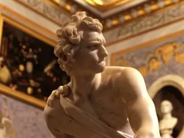 Bernini\'s David marble statue shown in a gallery interior, holding a sling and looking to the side.
