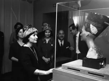 Bust of Nefertiti displayed in a glass case, with visitors gathered around it.