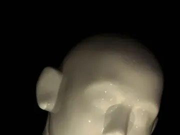 Close-up of Greetingman showing a bowed head and upper torso against a black background.