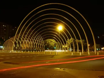 Puerta de la Ilustración lit with golden arches curving into a tunnel-like structure at night, with red light trails on the pavement.