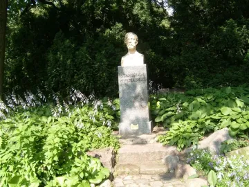 Bust of Stanisław Wyspiański on a dark pedestal in a green garden