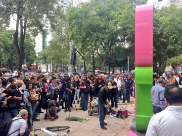 Antimonumento 49 ABC in a public plaza, with people photographing and filming as someone uses power tools at its base.
