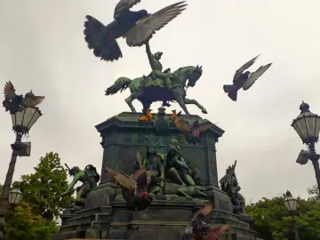 Dom Pedro I Equestrian Statue on a sculpted pedestal, with pigeons flying around it and ornate lampposts nearby.