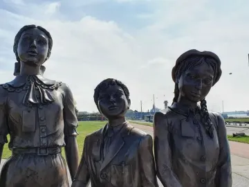 Kindertransport bronze sculpture of three children standing outdoors near a road and grassy area.