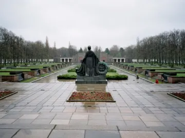 The Soviet War Memorial Schönholzer Heide statue seen from behind, holding a wreath over a wet paved plaza.