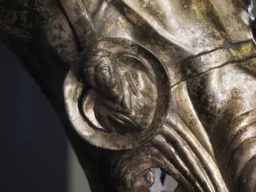 Close-up of the Waldgirmes Horse\'s Head showing a bronze-toned circular medallion with a profile head and decorative folds around it.
