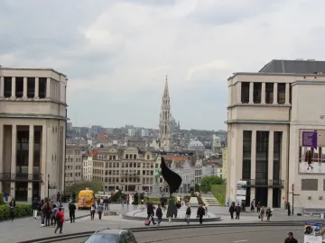 The Whirling Ear sculpture in a circular plaza with people walking nearby and a city skyline in the background.